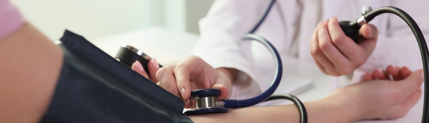 Medical provider measuring blood pressure of a patient in clinic that offers HIV medical care, STI testing, PrEP and general primary care.